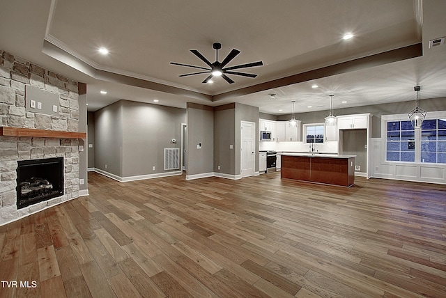 unfurnished living room with hardwood / wood-style flooring, ceiling fan, a fireplace, ornamental molding, and a raised ceiling