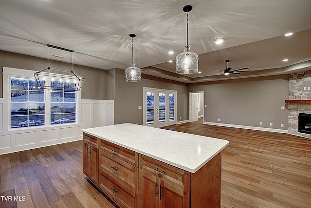 kitchen featuring french doors, a stone fireplace, decorative light fixtures, a center island, and light wood-type flooring