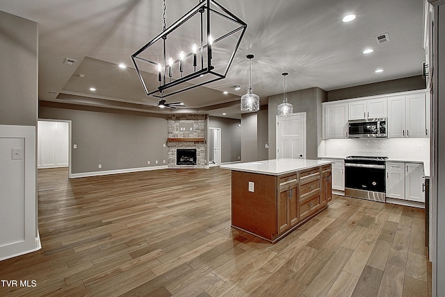 kitchen featuring appliances with stainless steel finishes, a stone fireplace, decorative light fixtures, white cabinetry, and a center island