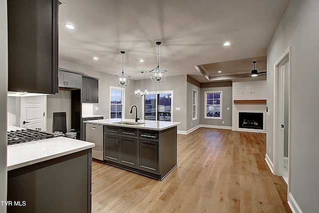 kitchen featuring appliances with stainless steel finishes, an island with sink, sink, hanging light fixtures, and light hardwood / wood-style flooring