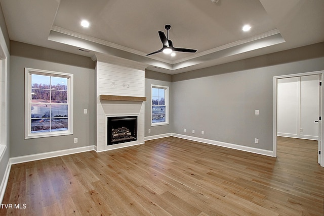 unfurnished living room featuring crown molding, ceiling fan, a tray ceiling, a fireplace, and light hardwood / wood-style floors