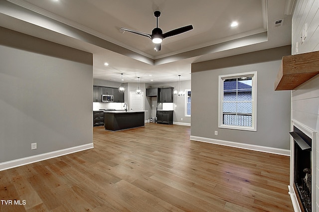 unfurnished living room with hardwood / wood-style floors, sink, ceiling fan, a raised ceiling, and crown molding