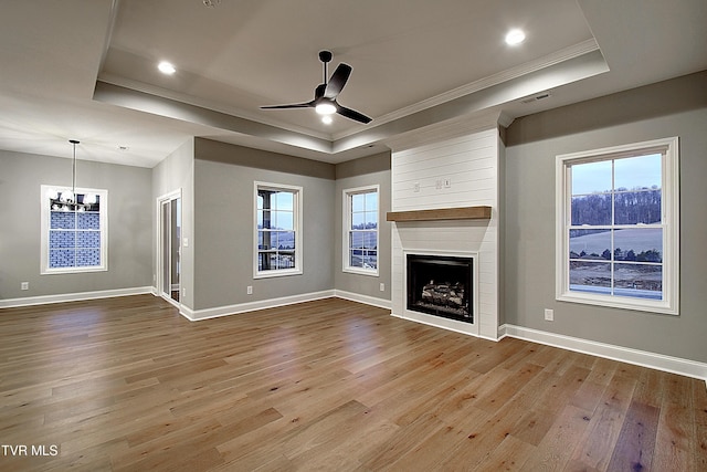 unfurnished living room with a large fireplace, ornamental molding, a tray ceiling, and light wood-type flooring