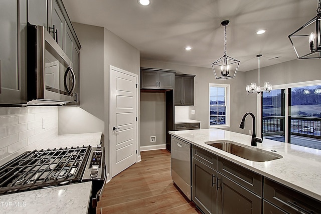 kitchen with pendant lighting, sink, stainless steel appliances, and light stone countertops