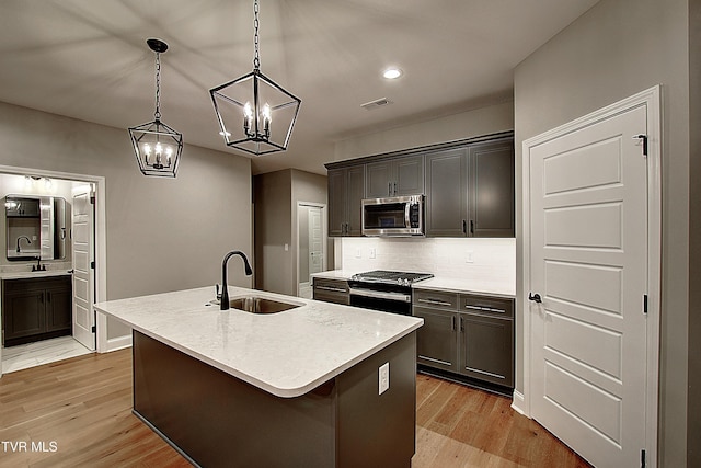 kitchen with sink, range with gas stovetop, light hardwood / wood-style floors, a center island with sink, and decorative light fixtures