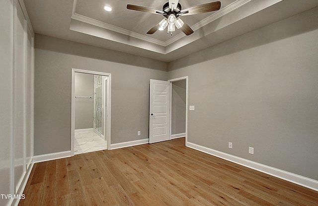 unfurnished bedroom featuring a raised ceiling, ornamental molding, ensuite bathroom, and light hardwood / wood-style floors