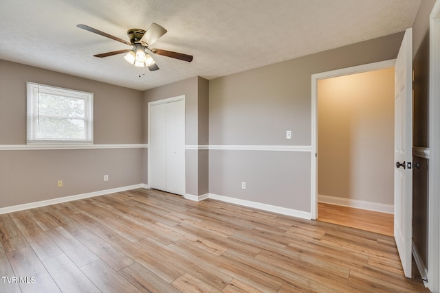 unfurnished bedroom with ceiling fan, a textured ceiling, light wood-type flooring, and a closet