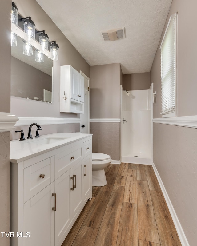 bathroom with a textured ceiling, walk in shower, hardwood / wood-style floors, vanity, and toilet