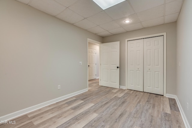 unfurnished bedroom with a closet, a drop ceiling, and light hardwood / wood-style flooring