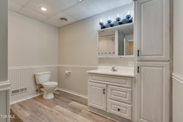 bathroom with a drop ceiling, hardwood / wood-style flooring, vanity, and toilet