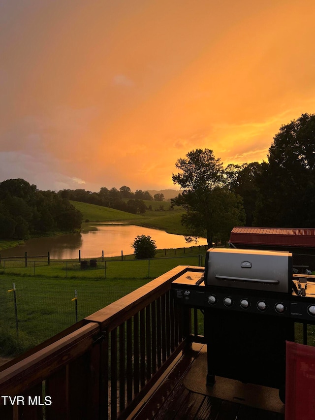 deck at dusk featuring a lawn, a water view, and a grill