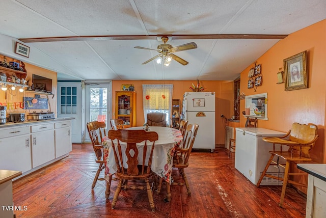 dining space with wood-type flooring, a ceiling fan, vaulted ceiling with beams, and a textured ceiling