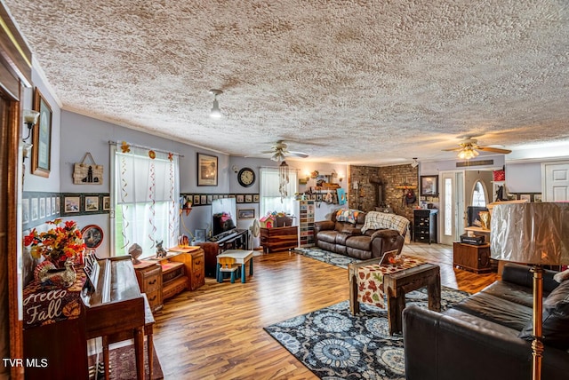 living room featuring a textured ceiling, wood finished floors, ceiling fan, and a wood stove