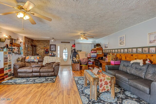 living room with light hardwood / wood-style flooring, wood walls, ceiling fan, and a textured ceiling