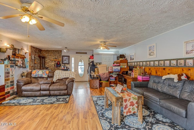 living room with a ceiling fan, a wood stove, a textured ceiling, light wood-type flooring, and ornamental molding