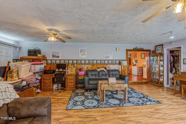 living room with light wood-type flooring, ceiling fan, and a textured ceiling