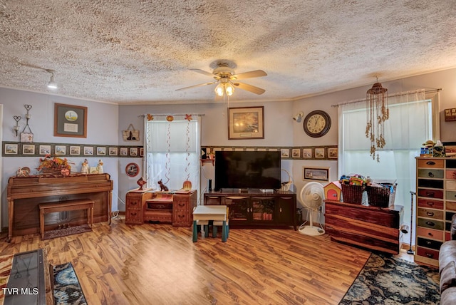living room featuring a ceiling fan, a textured ceiling, crown molding, and wood finished floors