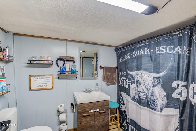 bathroom with a textured ceiling, wooden walls, vanity, and toilet