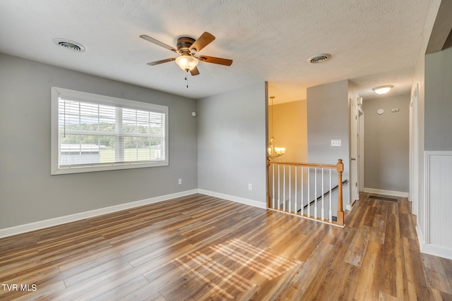 empty room featuring hardwood / wood-style flooring, ceiling fan with notable chandelier, and a textured ceiling