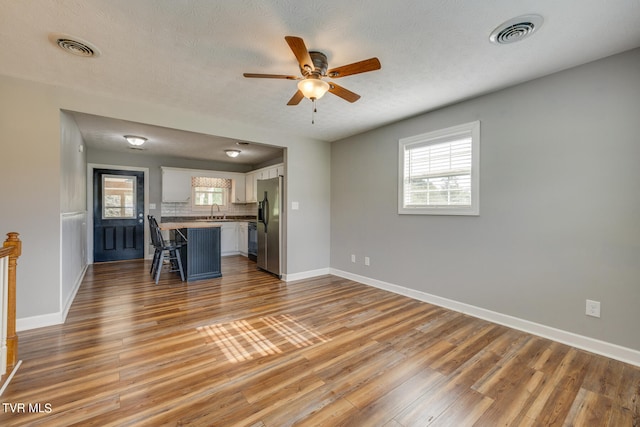 unfurnished living room with light hardwood / wood-style floors, plenty of natural light, ceiling fan, and a textured ceiling