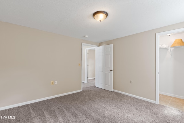 unfurnished bedroom with a spacious closet, a textured ceiling, light colored carpet, and a closet