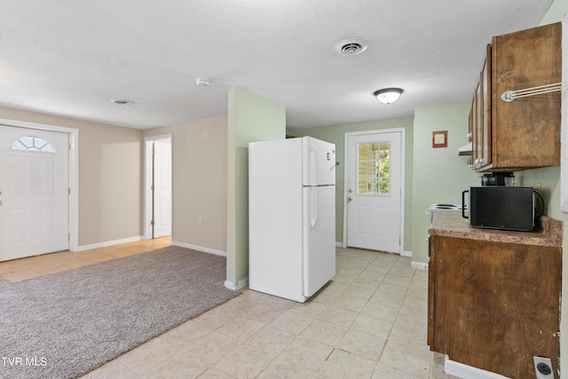 kitchen with stove, a textured ceiling, light colored carpet, and white refrigerator