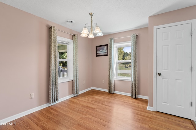 empty room with an inviting chandelier, light hardwood / wood-style flooring, and a textured ceiling