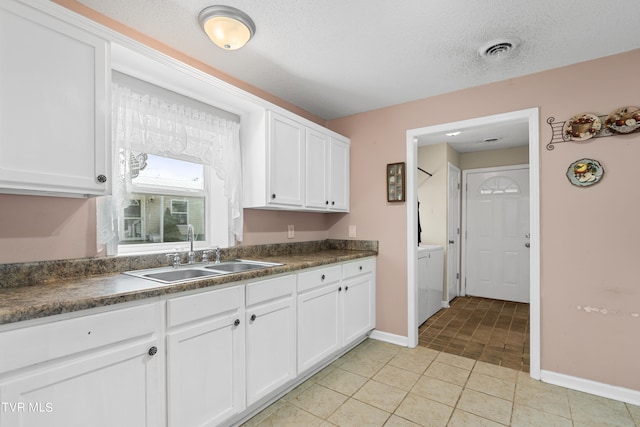 kitchen with white cabinets, sink, light tile patterned floors, and a textured ceiling