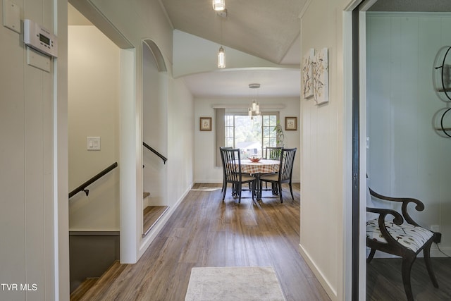 corridor with lofted ceiling, baseboards, wood finished floors, and arched walkways