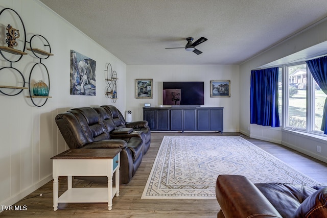 living area with baseboards, a ceiling fan, wood finished floors, and a textured ceiling