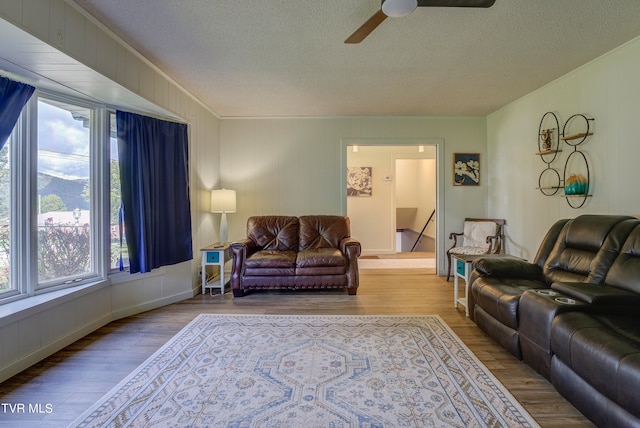 living room featuring ceiling fan, a textured ceiling, light wood-type flooring, and ornamental molding