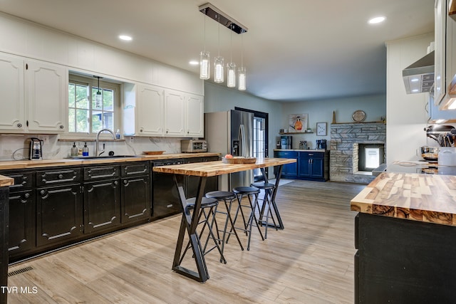 kitchen with decorative light fixtures, light wood-type flooring, wooden counters, and white cabinetry