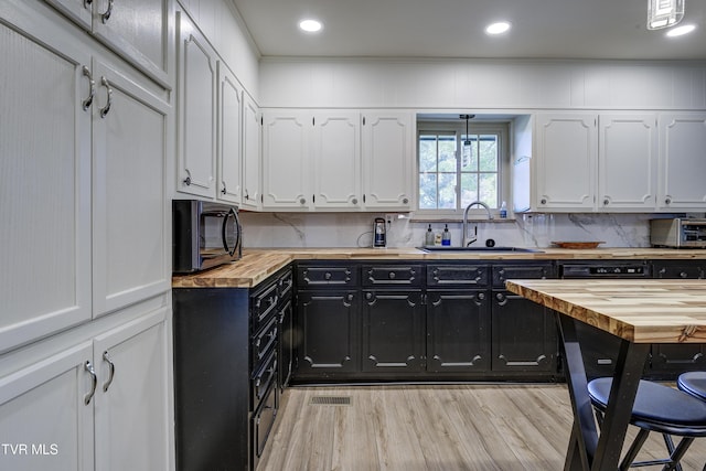 kitchen featuring white cabinets, dark cabinets, a sink, decorative backsplash, and butcher block countertops