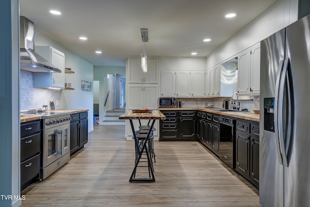 kitchen with wall chimney exhaust hood, light hardwood / wood-style flooring, butcher block counters, stainless steel appliances, and white cabinetry