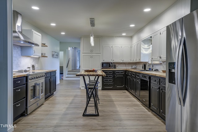 kitchen featuring a sink, wall chimney exhaust hood, decorative backsplash, appliances with stainless steel finishes, and white cabinetry