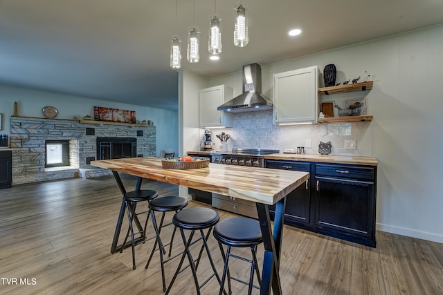 kitchen featuring white cabinets, wall chimney exhaust hood, wooden counters, pendant lighting, and a fireplace