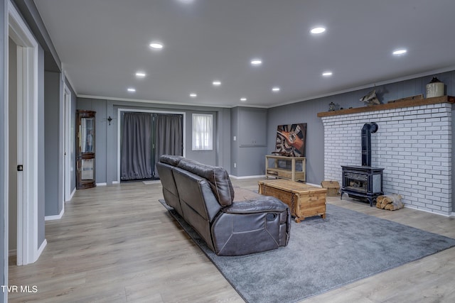 living area featuring light wood-type flooring, a wood stove, baseboards, and ornamental molding