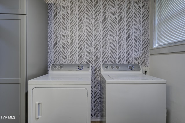 clothes washing area with wallpapered walls, washer and clothes dryer, and laundry area