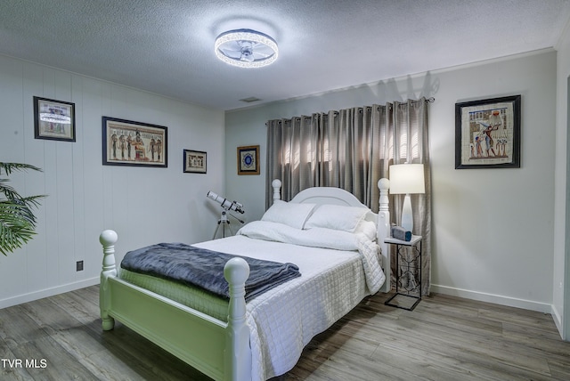 bedroom with baseboards, visible vents, wood finished floors, and a textured ceiling