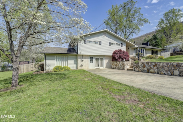 view of front facade featuring a front lawn, brick siding, fence, and driveway