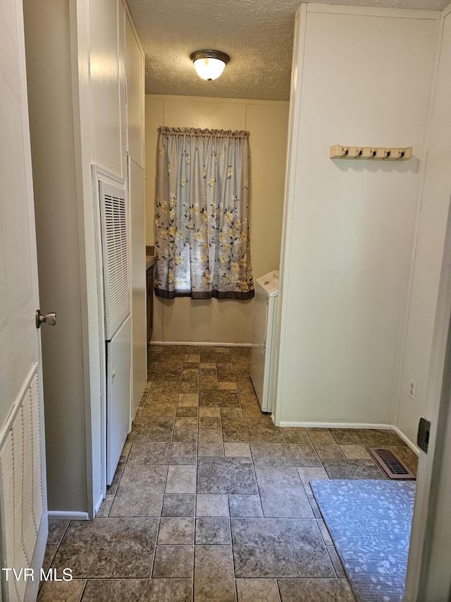 corridor with washer / dryer and a textured ceiling