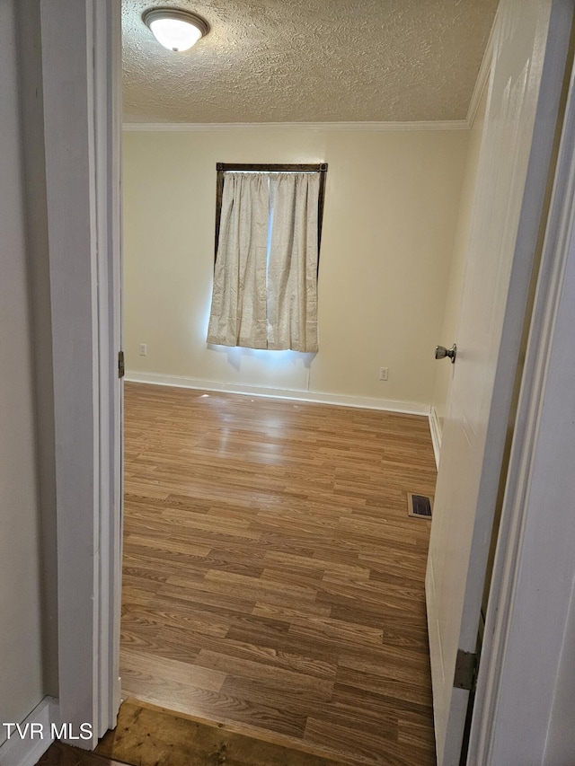 spare room featuring ornamental molding, wood-type flooring, and a textured ceiling