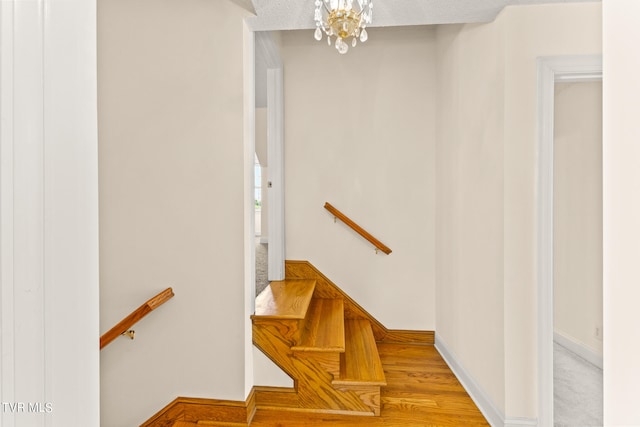 staircase featuring wood-type flooring, a notable chandelier, and a textured ceiling