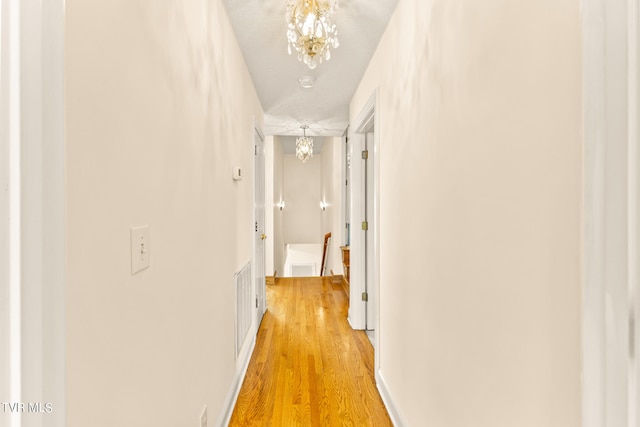 corridor with a notable chandelier, light wood-type flooring, and a textured ceiling