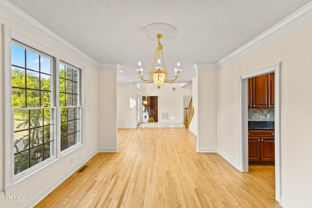 unfurnished dining area with light wood-type flooring, crown molding, an inviting chandelier, and a textured ceiling