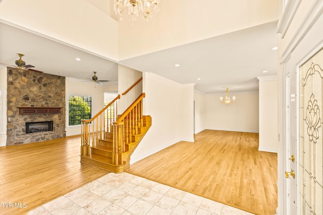 entryway with a stone fireplace, crown molding, ceiling fan with notable chandelier, a towering ceiling, and light hardwood / wood-style floors