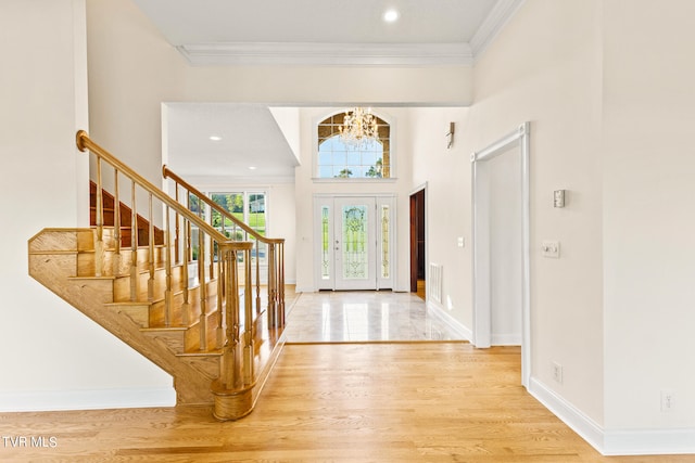 foyer entrance featuring a towering ceiling, a notable chandelier, crown molding, and hardwood / wood-style flooring