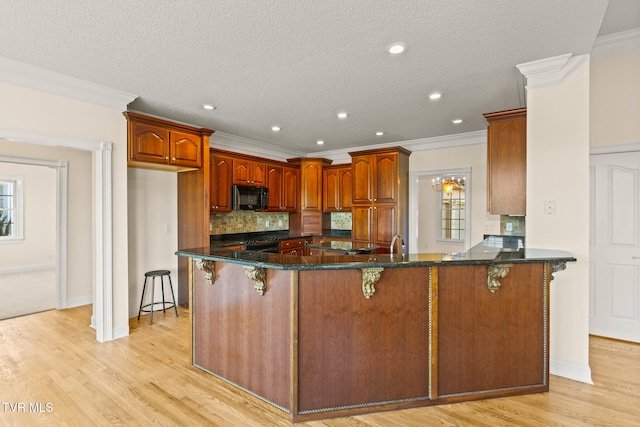 kitchen with dark stone counters, a kitchen bar, light wood-type flooring, and a textured ceiling