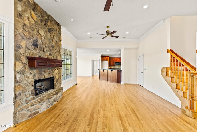 unfurnished living room with crown molding, ceiling fan, a fireplace, and light hardwood / wood-style floors