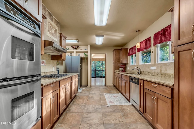 kitchen with light stone countertops, decorative backsplash, stainless steel appliances, sink, and decorative light fixtures